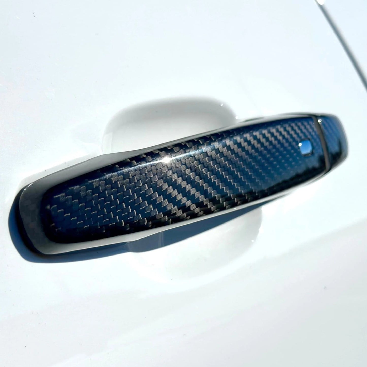 Rebel Carbon Fiber door handle cover with a glossy weave pattern installed on a white Chevrolet Camaro exterior
